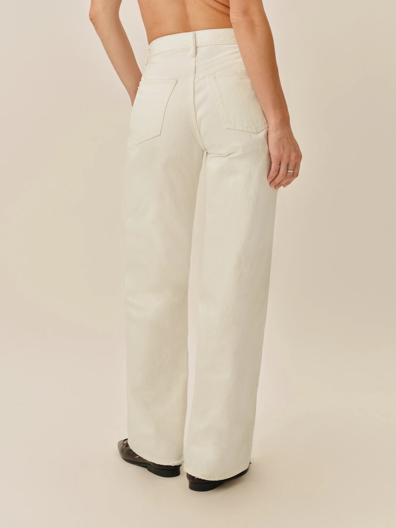 Person wearing high-waisted, off-white, straight-leg jeans with back pockets, viewed from behind against a plain background.