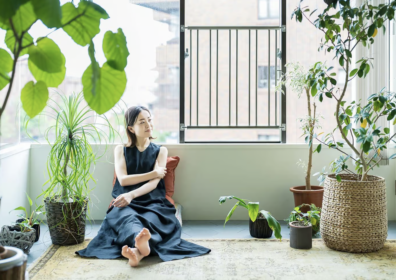 A woman sits on a glass patio among plants. 