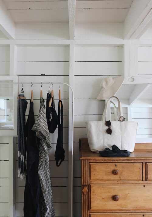 A garment rack in a white room next to a wooden dresser with a back and accessories on top. 