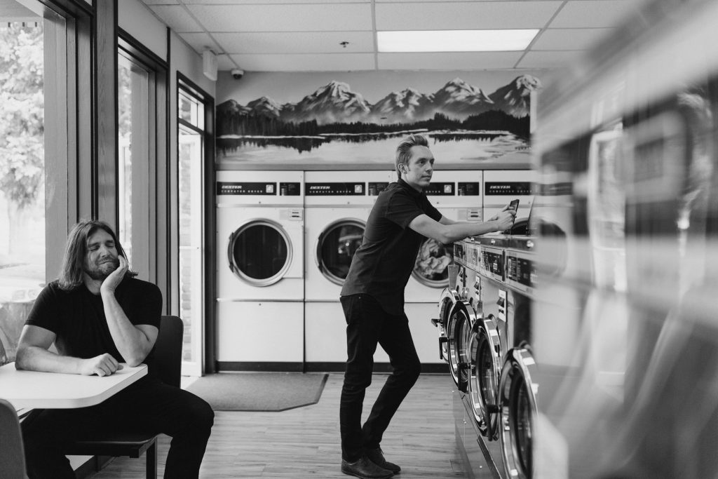 A black and white photo of an adult man in a laundromat. 