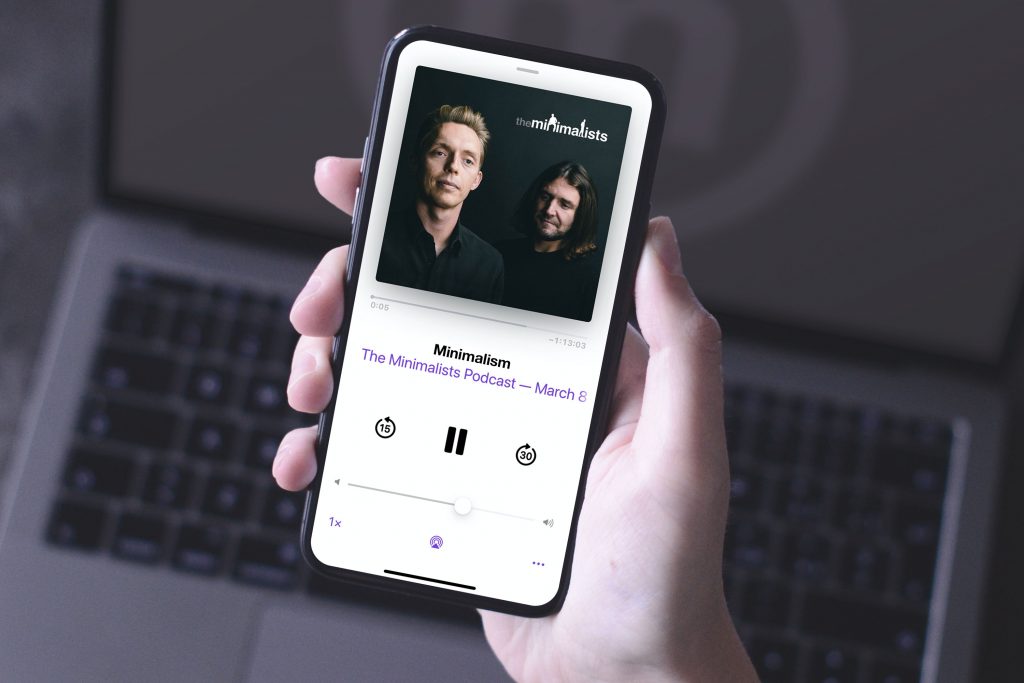 A hand holds a phone with the Minimalists' podcast on the screen. 