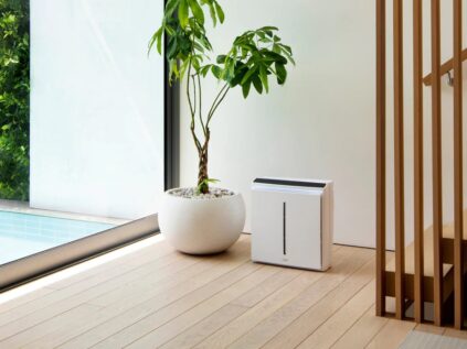 A modern air purifier beside an indoor plant in a minimalist home interior.