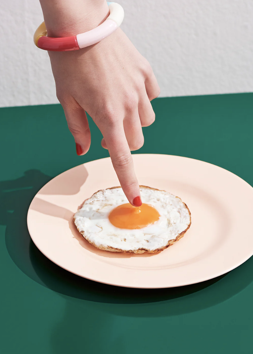 A photo of a hand reaching down to touch the yolk of a fried egg.