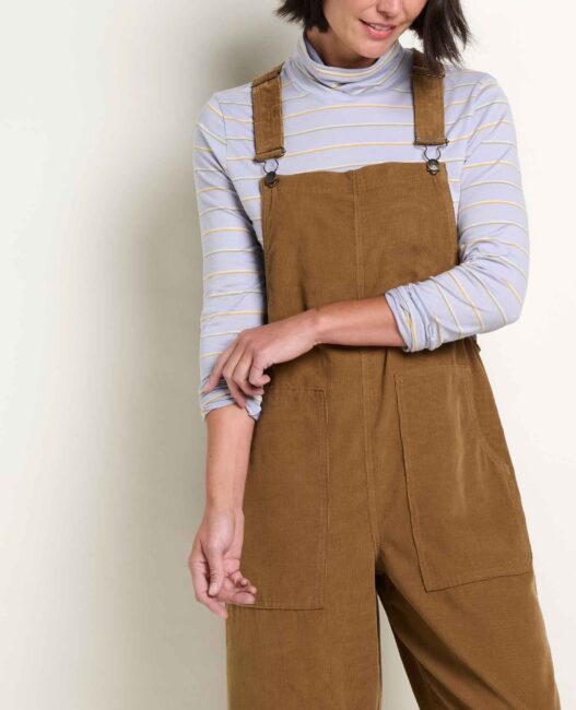 A person wearing brown overalls over a light blue and yellow striped turtleneck.
