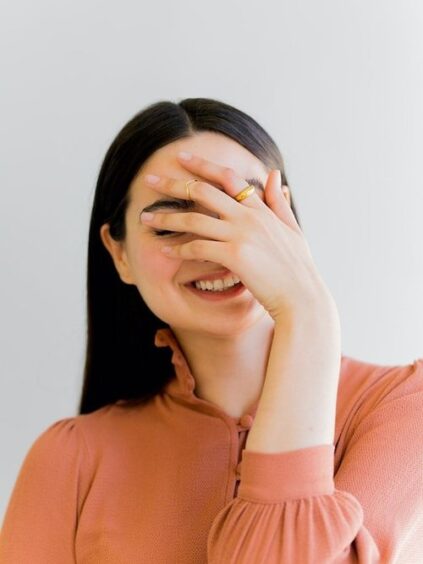 Smiling woman covering her face with her hand against a white background.