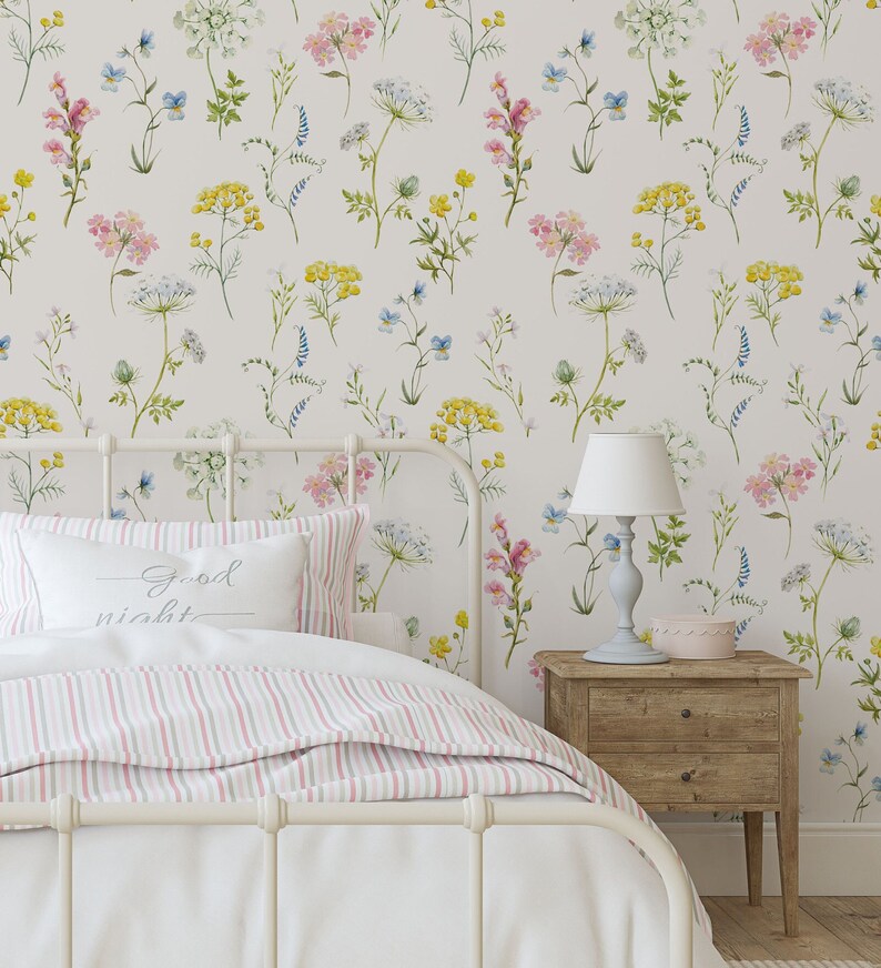 A cozy bedroom with floral wallpaper, a white bed with striped bedding, and a wooden bedside table with a lamp.