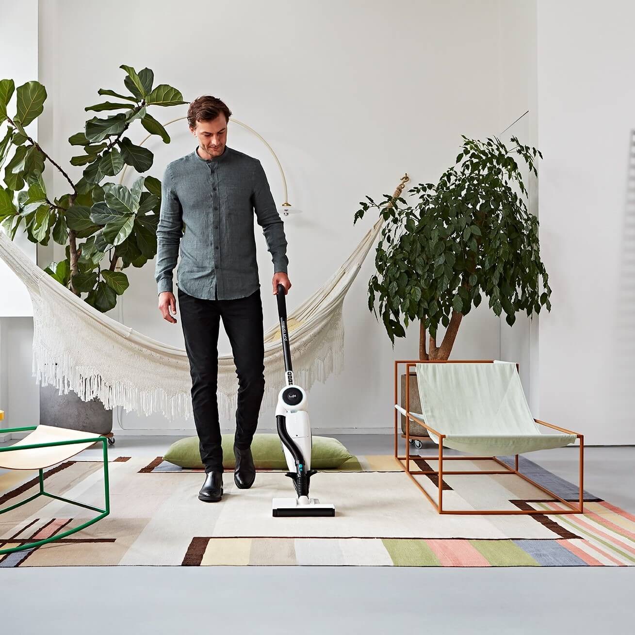 A man vacuuming a room with modern decor and a hammock.