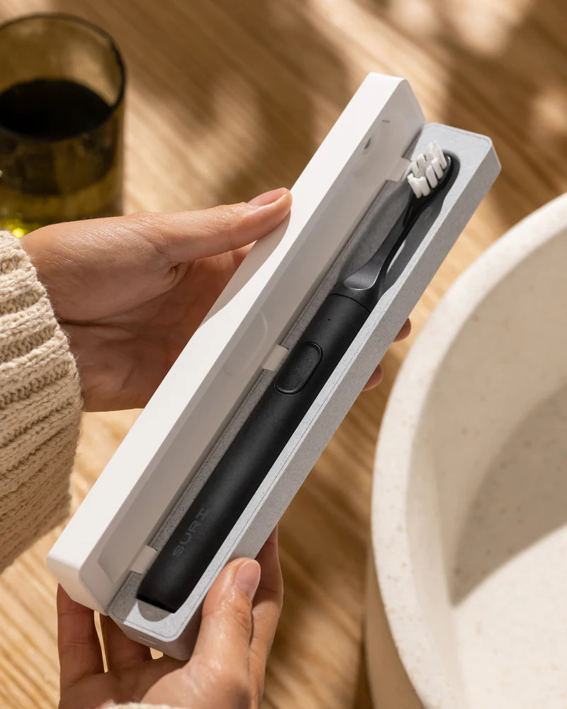 A hand opening a box with a SURI Sustainable Electric Toothbrush