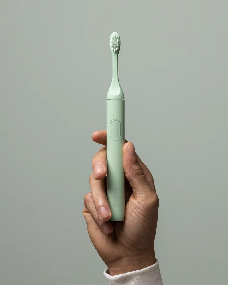 A hand holding a SURI Sustainable Electric Toothbrush