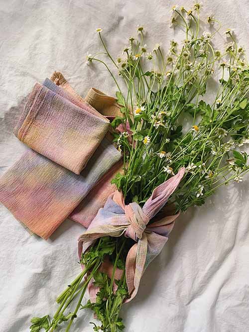 Cloth Napkins: Apricot's tie-dyed watercolor dinner napkins are layered on top of another next to a bouquet of flowers tied together with a napkin.