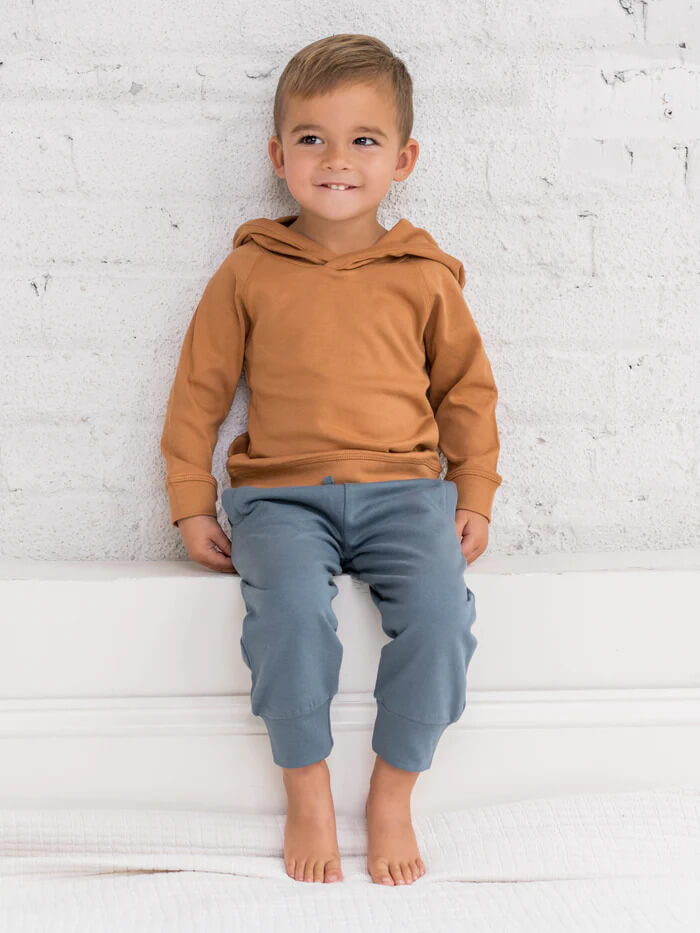 A young boy in a camel colored hoodie and blue joggers.