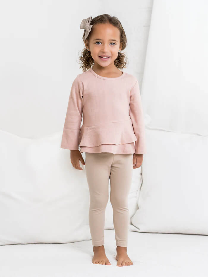 A young girl in a pink top and tan leggings.