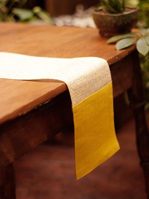 Tablecloths & Runners: Kiriko's Ban Inoue Table Runner in Yellow Waves hangs off of a brown table.