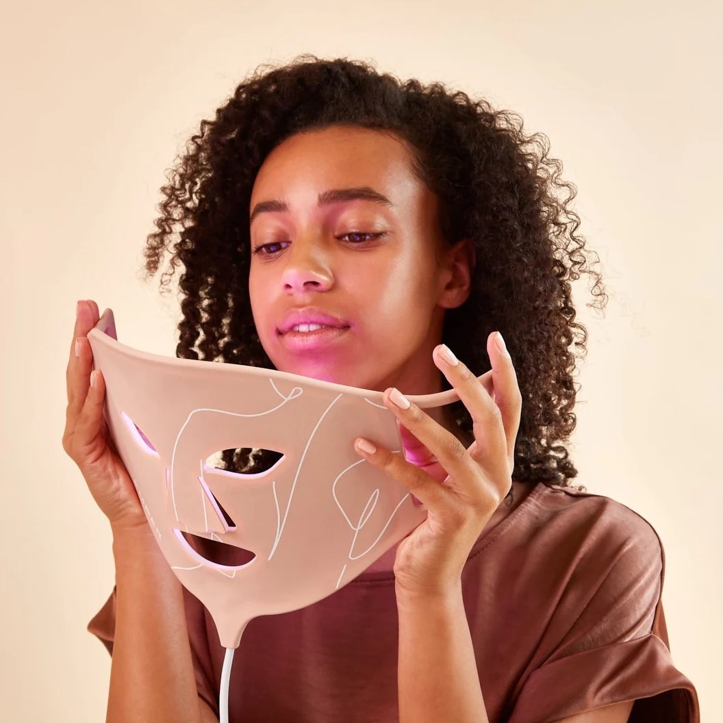 A model lifts a red light mask to her face.