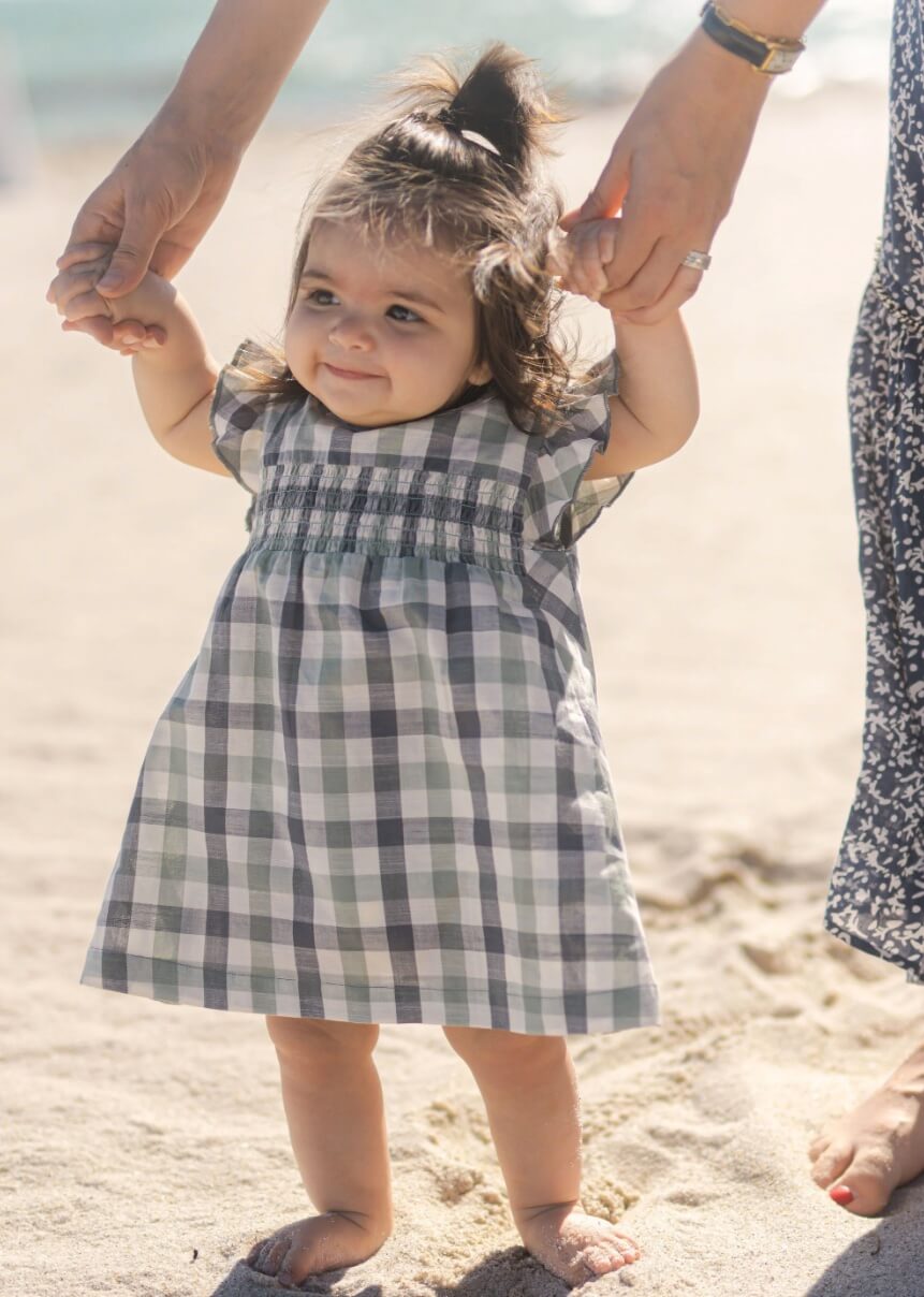 A baby wearing a plaid checkered dress from Pehr.