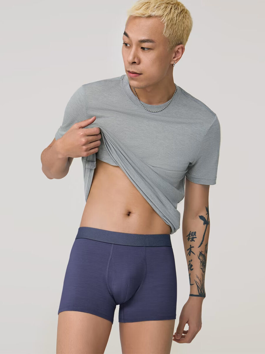 A model holds up his gray t-shirt to show off his blue boxer briefs.