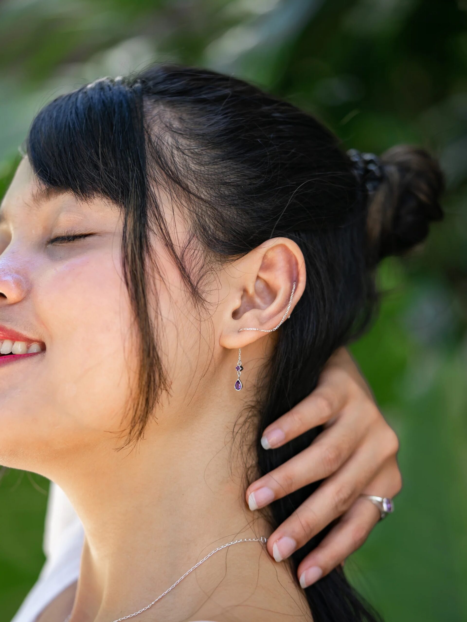 Woman smiling with closed eyes, showcasing an earring and touching her neck.