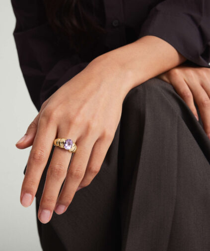 Close-up of a woman's hand resting on her lap, adorned with a large purple gemstone ring.
