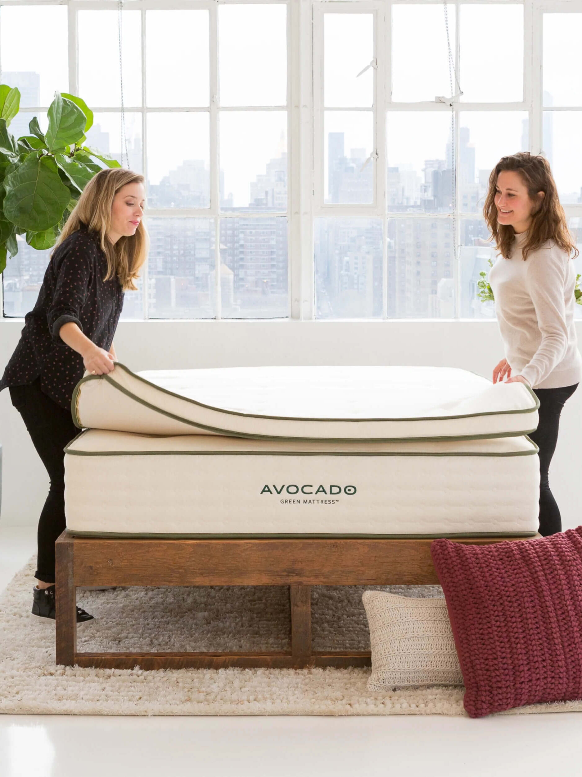 Two models place an Avocado organic mattress topper on top of a mattress.