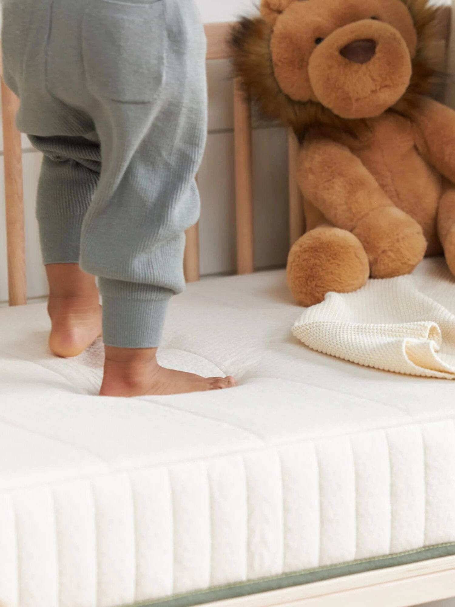 A child's feet stand on an Avocado crib mattress