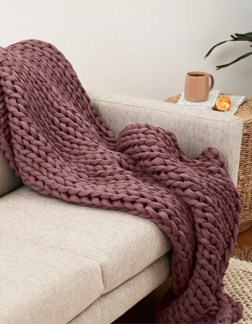 Maroon Bearaby weighted blanket thrown across a cream couch.