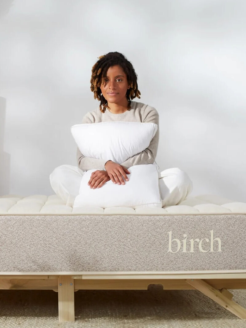 A woman sits on her Birch natural latex mattress hugging a pillow to her chest.