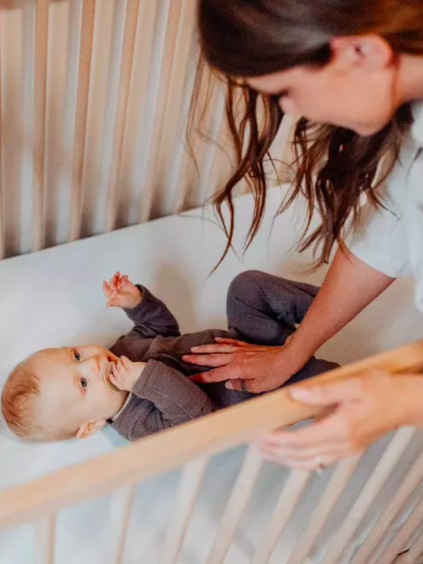 A woman bends over a Colgate crib mattress and puts her hand on a baby's belly