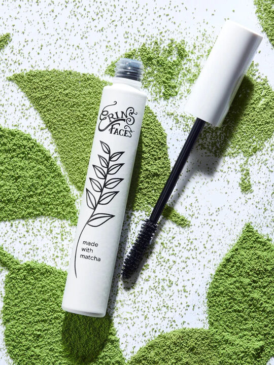 Erin's Faces Matcha Mascara with powdered matcha in the shade of leaves behind the product.