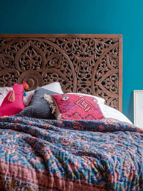 An intricately carved wooden headboard and colorfully made bed.