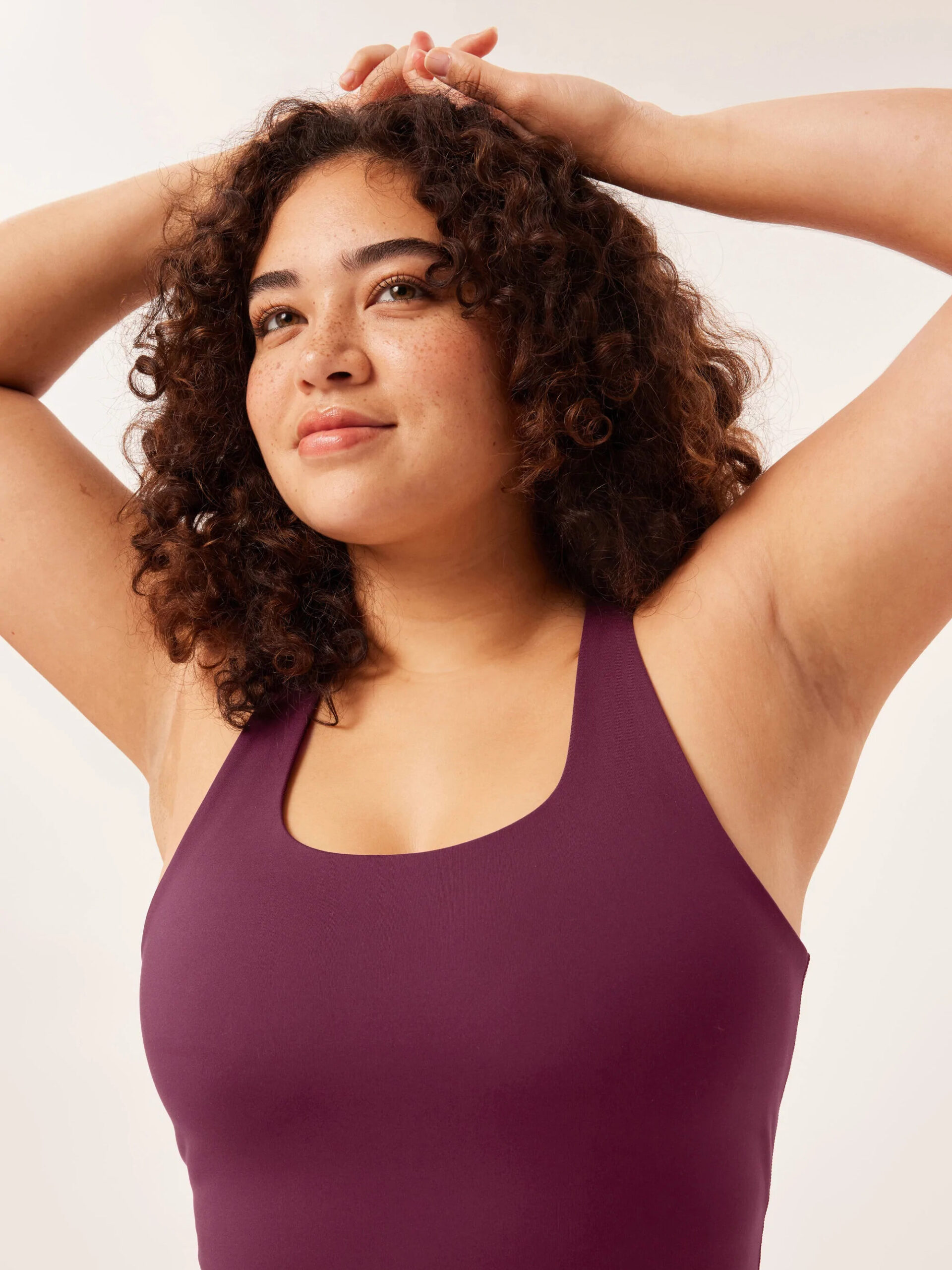 Model wearing a plum sports bra holds her arms over her head