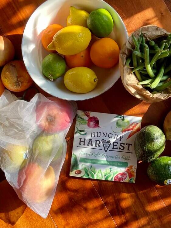 An overhead shot of a table with a bowl of fruit and vegetables and a piece of paper that says Hungry Harvest on it.