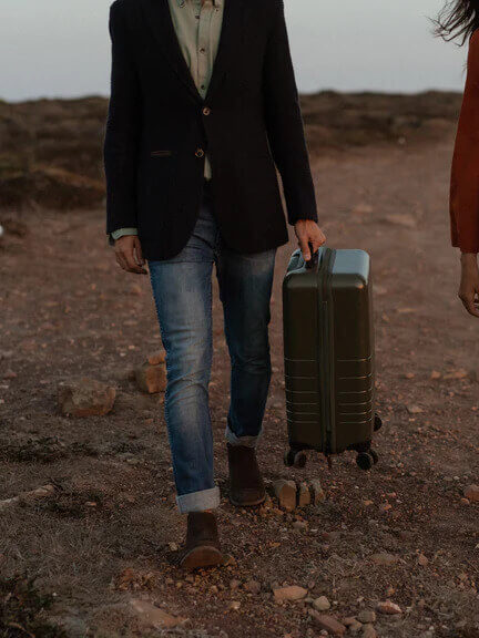 A model carries a case through a dirt road. 