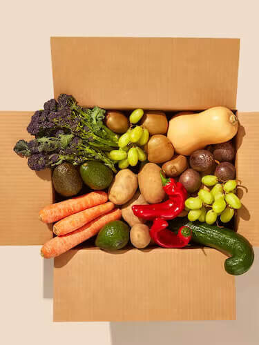 An open cardboard box filled with vegetables and fruits.