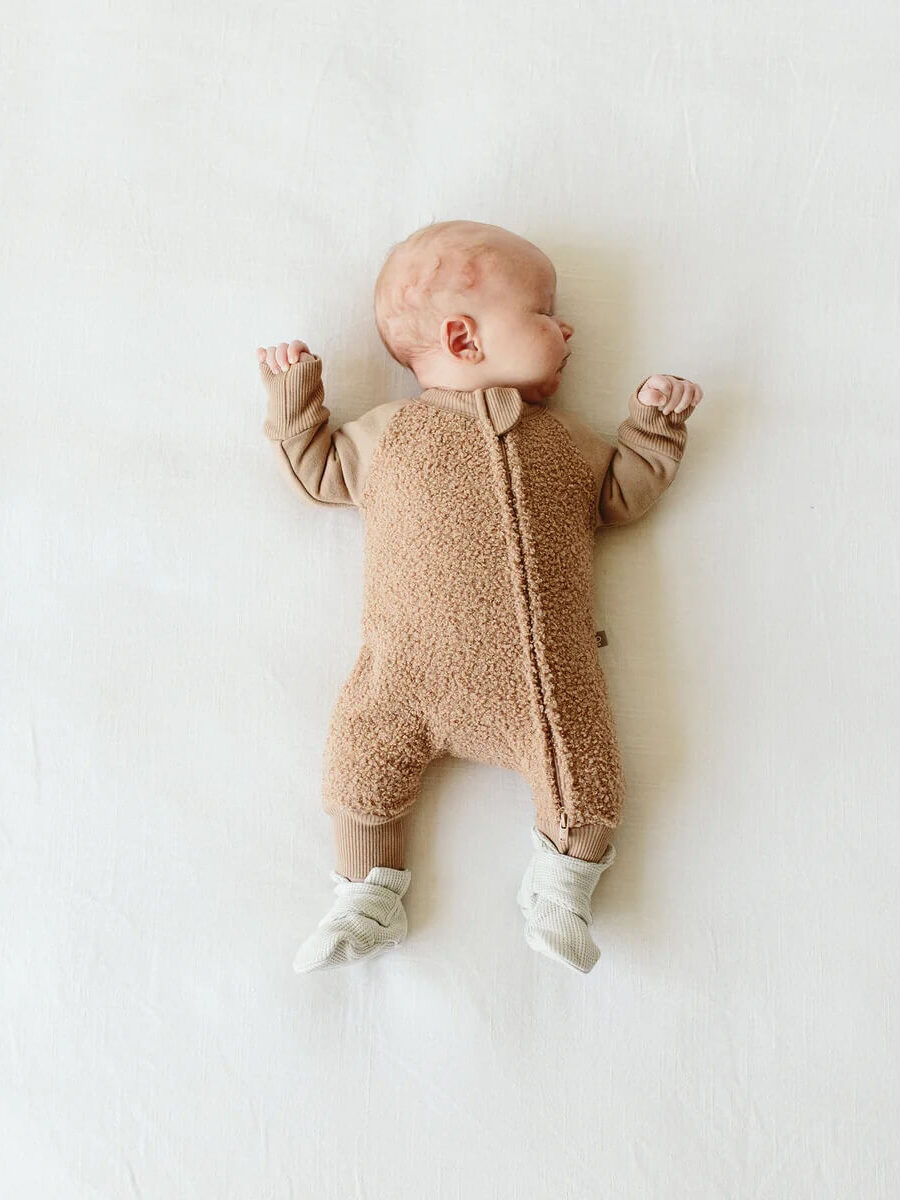 A newborn wearing a fuzzy beige onesie from Goumi.