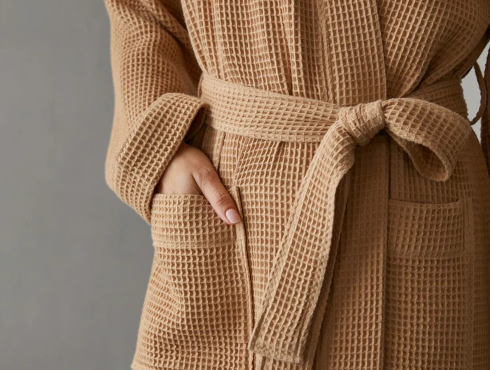 A closeup of the waist area of a person wearing a Coyuchi beige waffle knit robe, with their hand in the pocket.
