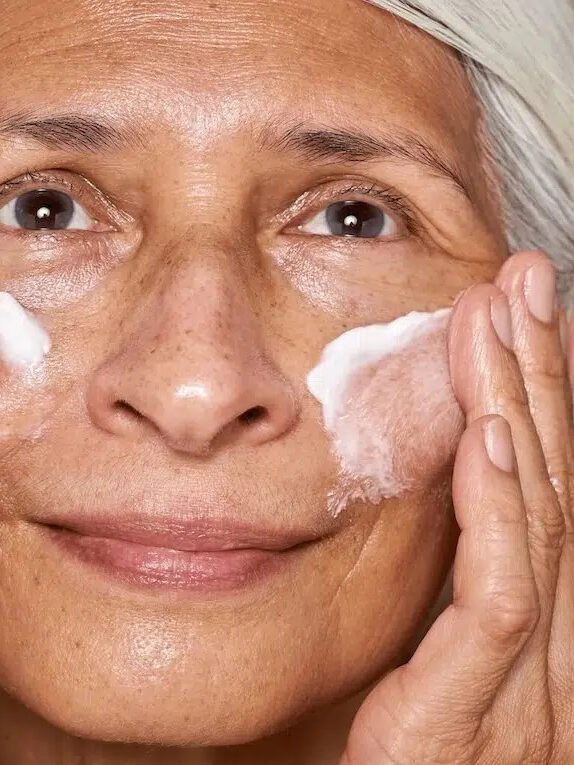 A closeup of a woman's face applying Osea skincare.