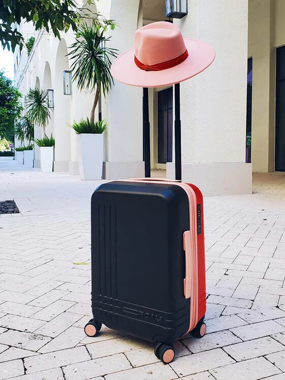 A navy, pink, and red suitcase with a pink fedora on its handle. 