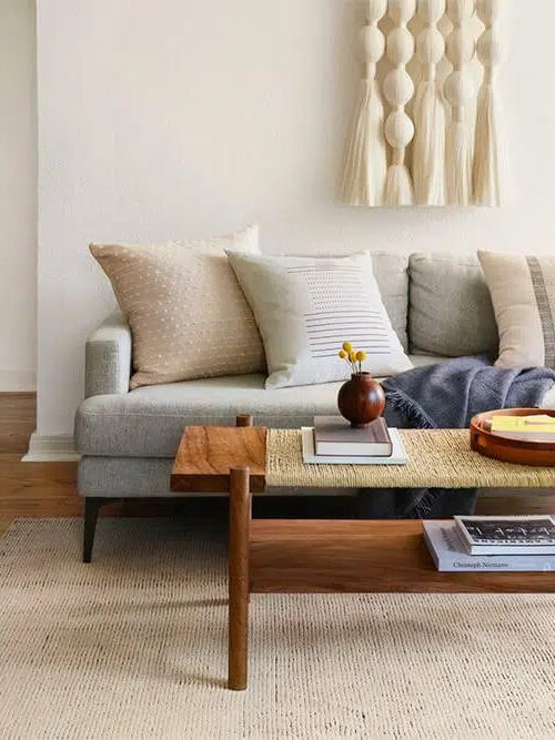 A gray couch and wooden coffee table with a woven top.