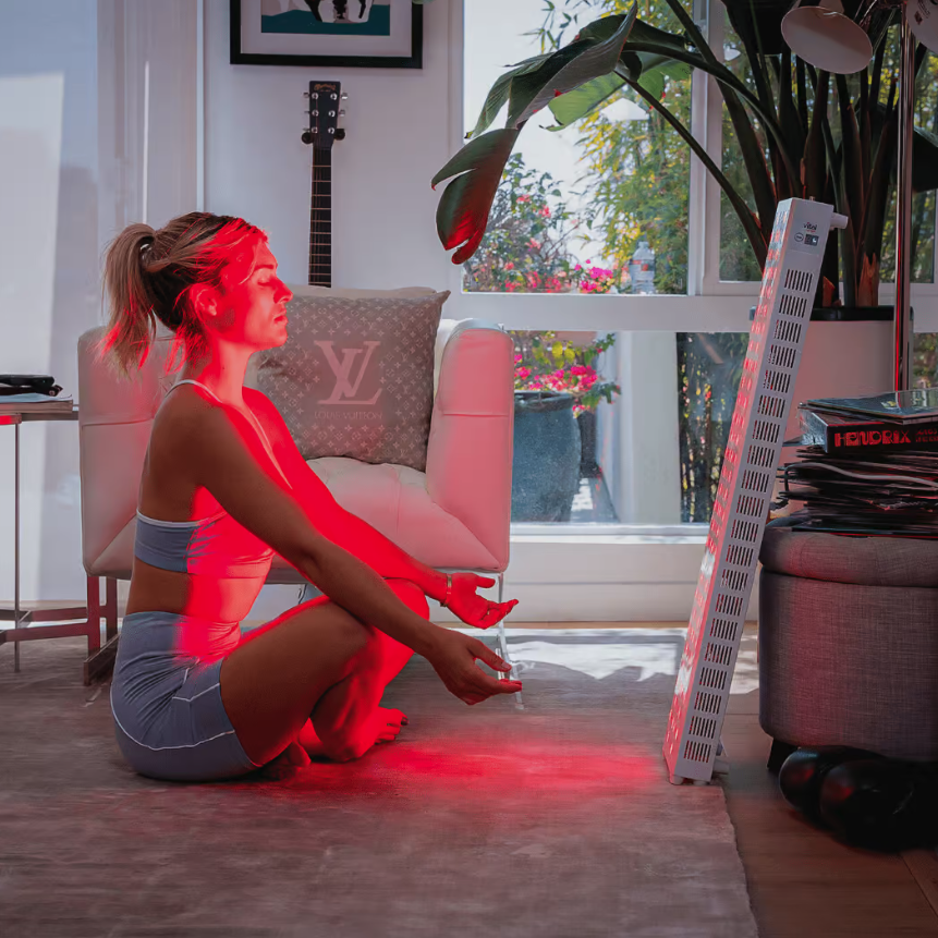 A woman sits in front of a red light device.