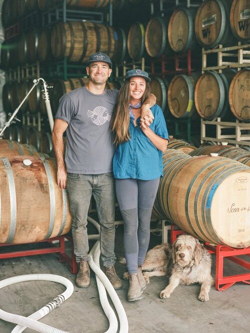 A couple in a wine barrel warehouse with a dog at their feet.