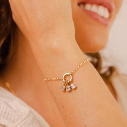 A close-up of a woman's wrist wearing a delicate bracelet with small gemstone charms, smiling in the background.