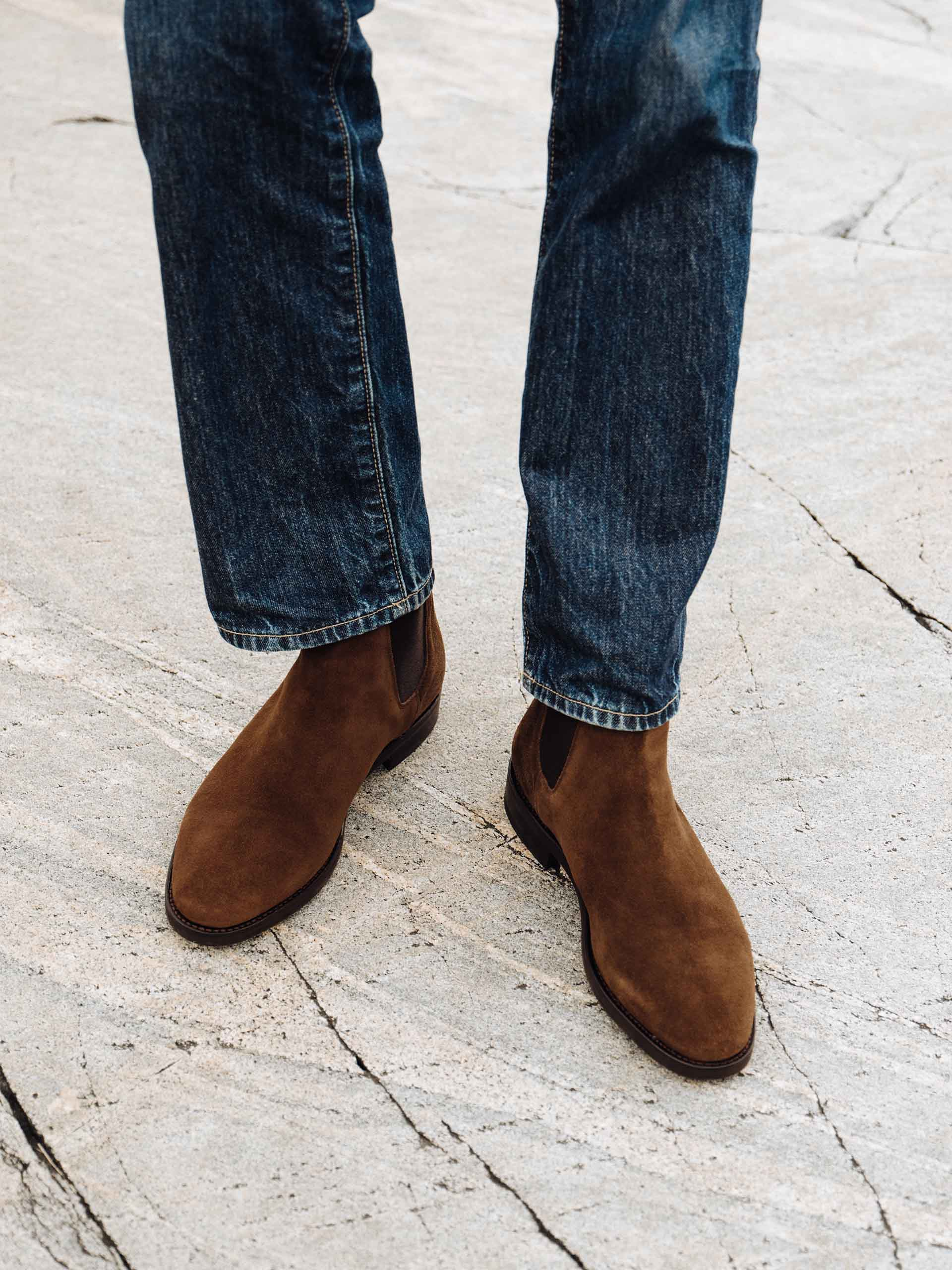 A pair of legs wearing dark blue jeans and brown MORJAS boots.