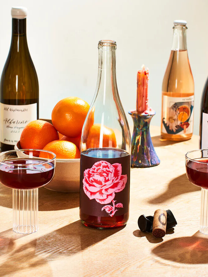 Bottles of wine and glasses of wine on a table with bowls of fruit and candles.