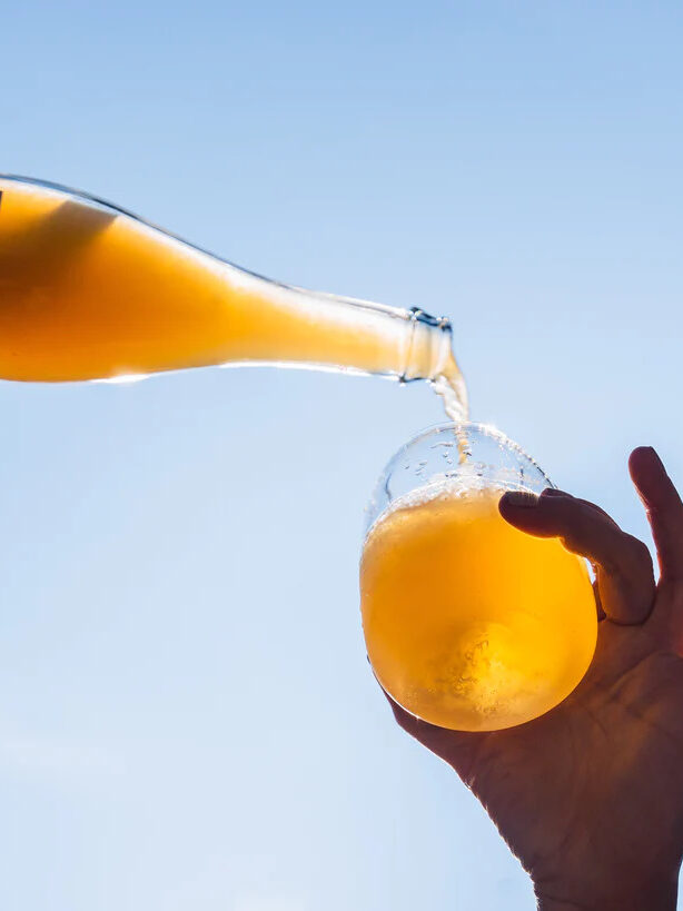 A hand pours a bottle of orange wine into a glass from below.