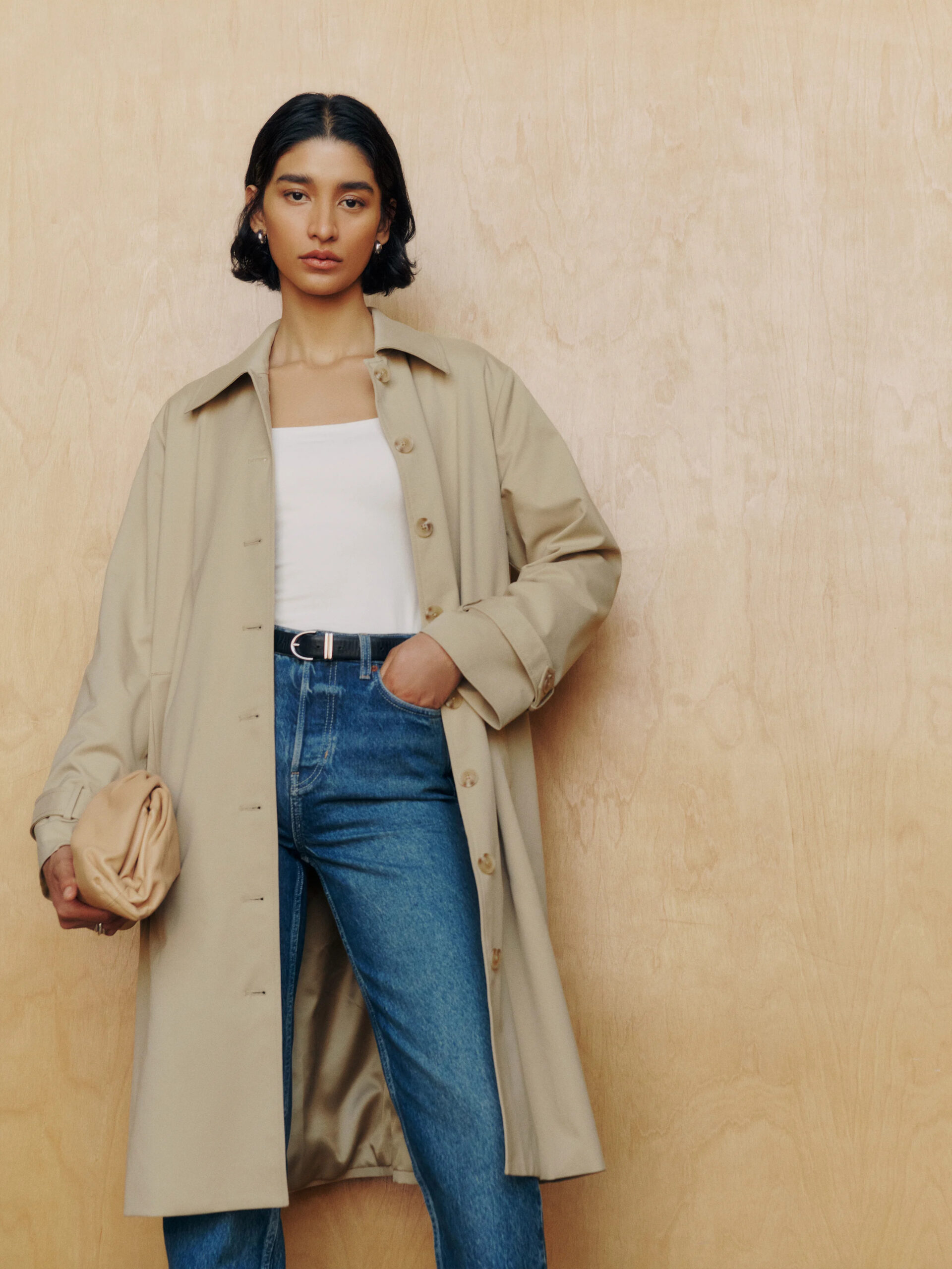 A model wearing a Reformation trench coat in a camel color.