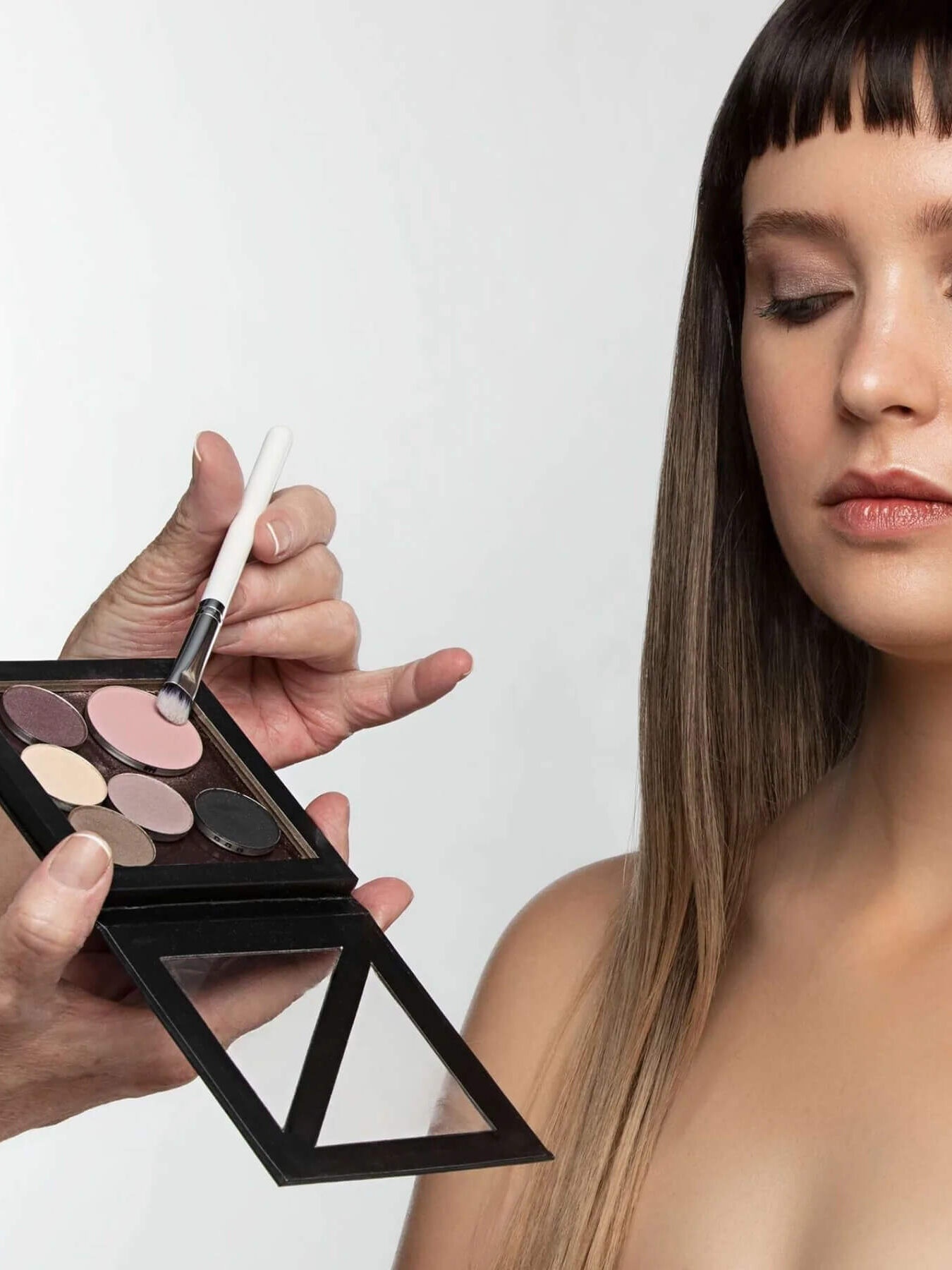 A hand applies a brush to Sappho natural eyeshadow palette and prepares to put it on a model. 