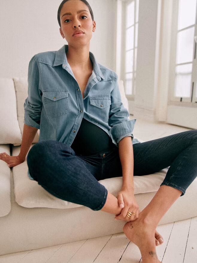 A pregnant woman in jeans and a denim shirt. 