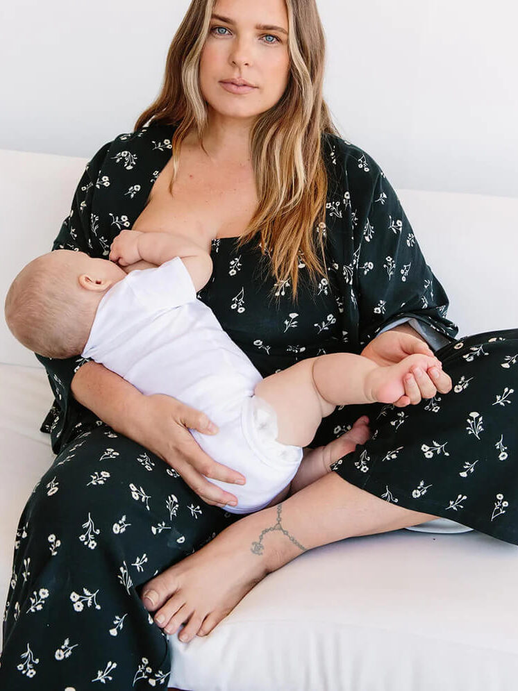 A model nurses her baby in a printed jumpsuit.