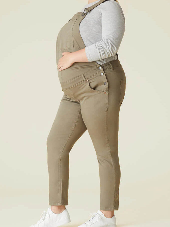 A pregnant person's torso wearing olive colored overalls.