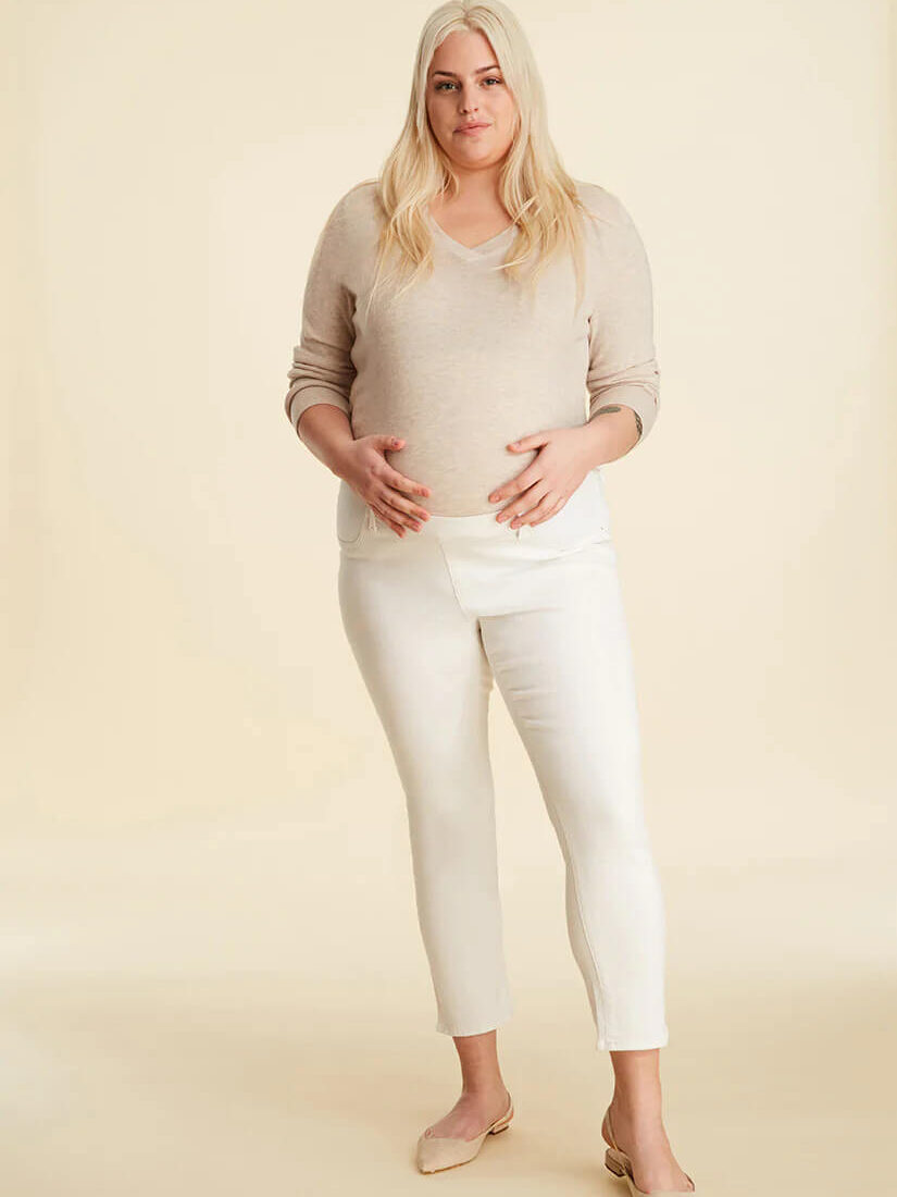 A pregnant person wearing cream jeans and beige sweater.